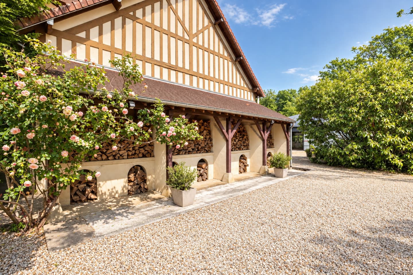 La cour de gravier et le bâtiment à colombage, ses rosiers en fleurs le long du mur